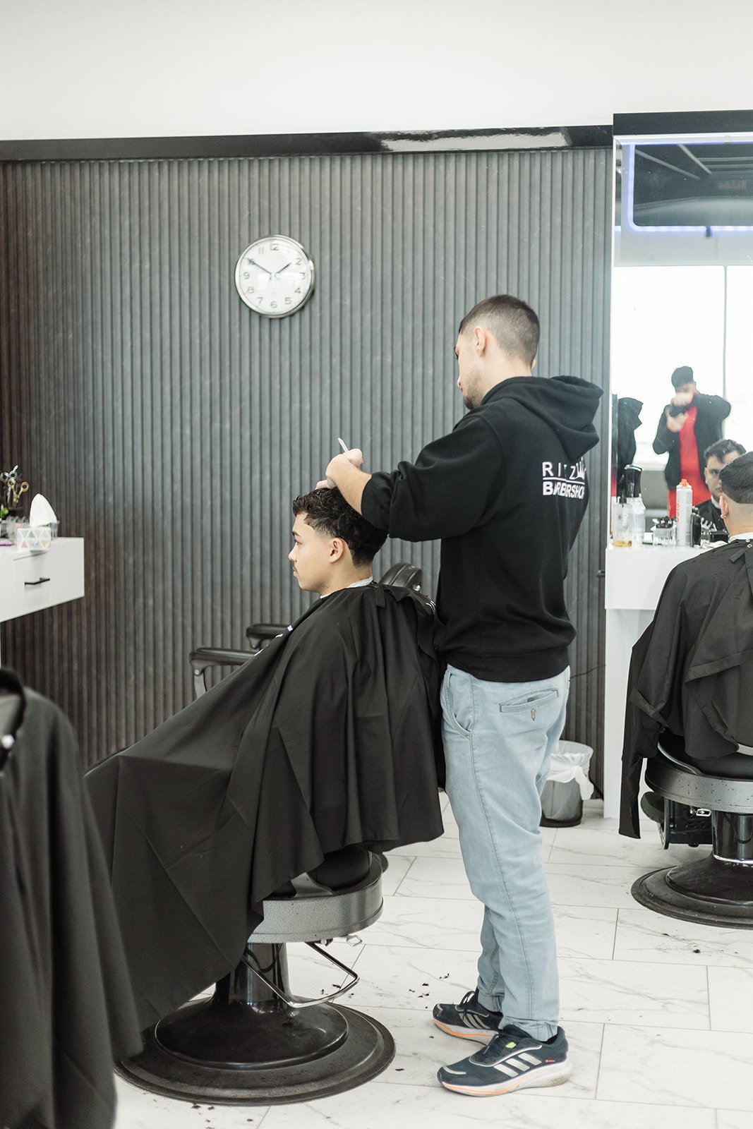 Barber in black Ritz hoodie working with shears and comb